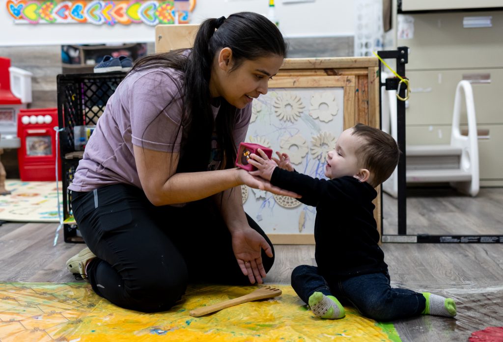 Educator offering a block to a toddler