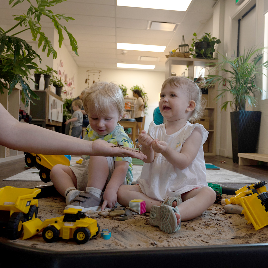 Two toddlers exploring sensory sand play with trucks.